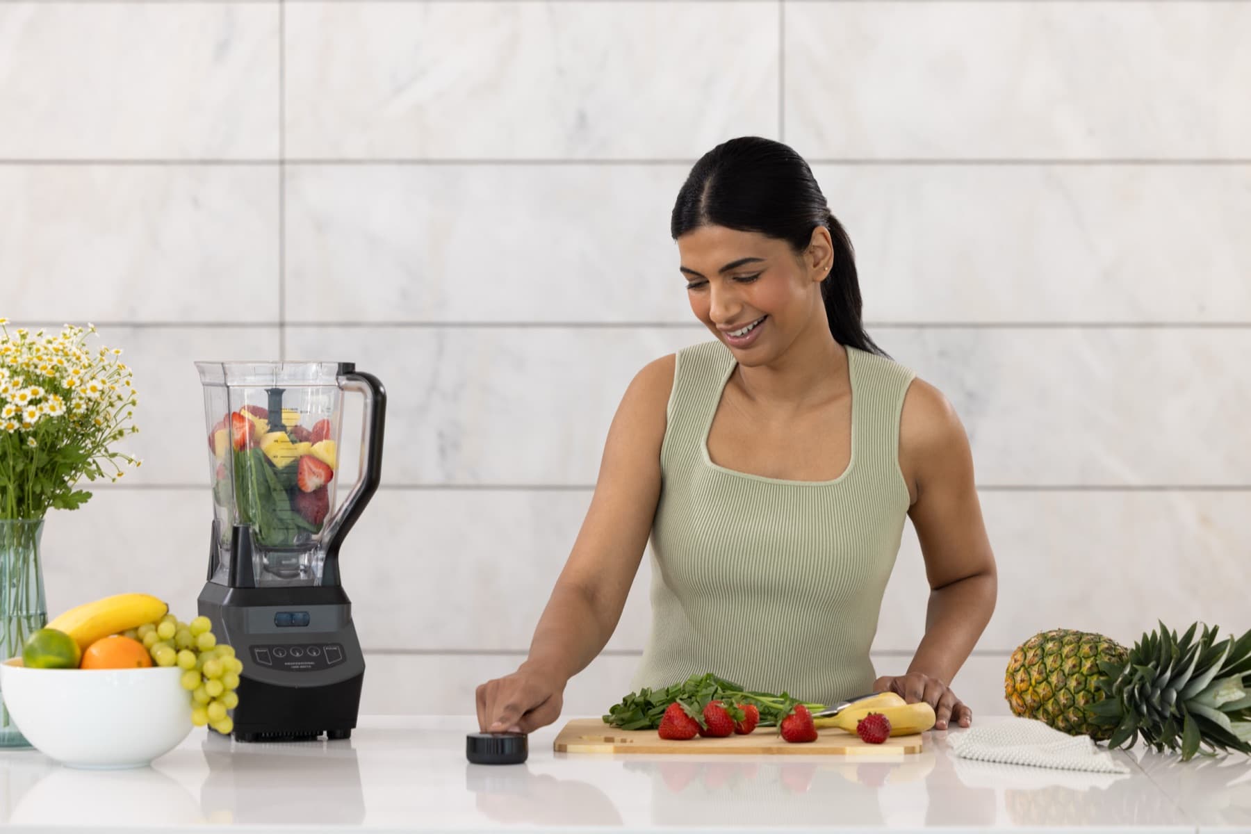 A woman smiling as she touches the Prysm iO scanner on a kitchen counter beside a blender of fruit and greens